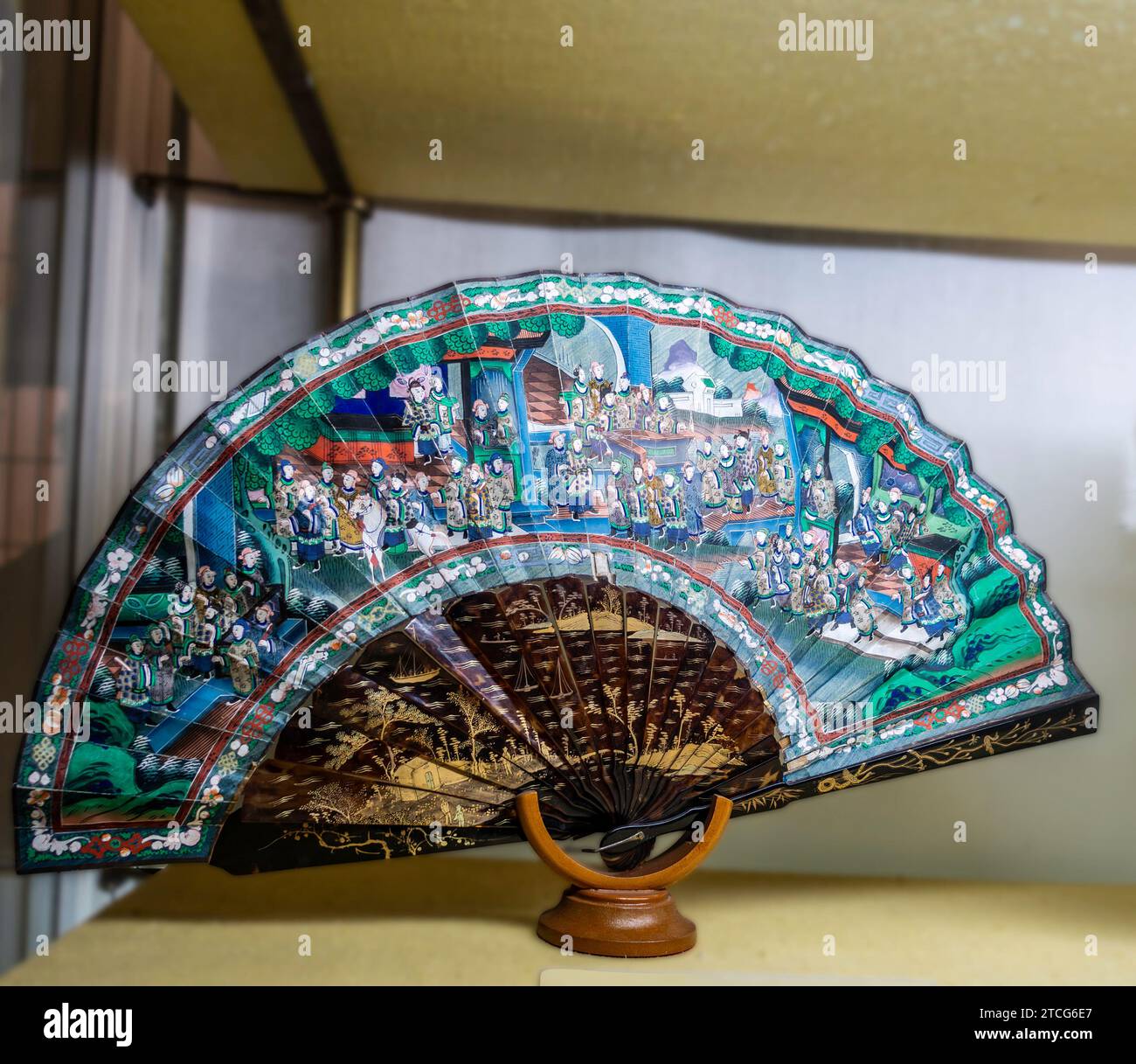 Colourful hand fan with detailed Asian artwork on stand displayed in the Alcázar of Seville, The Royal Palace of Seville, Spain. Stock Photo