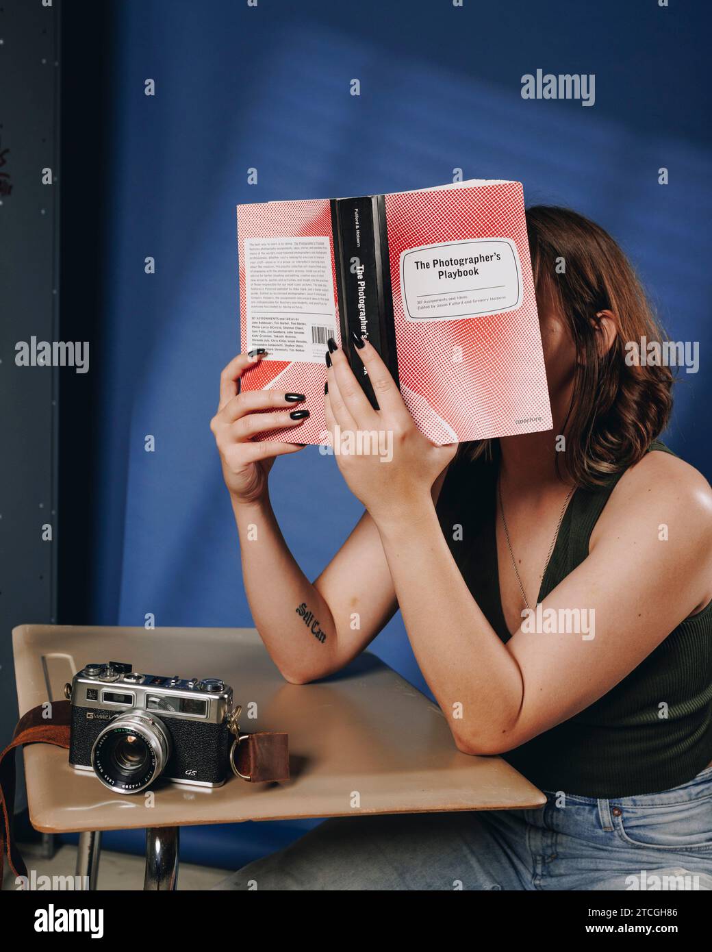college aged student sitting at a school desk with her face in textbooks Stock Photo