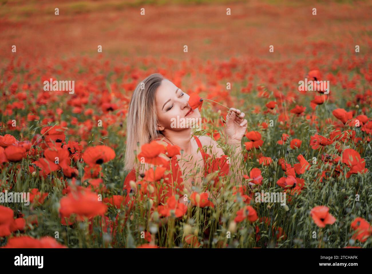 Happy woman in a red dress in a beautiful large poppy field. Blond sits ...