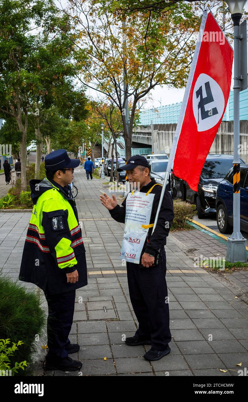 Taipei. 13th Dec, 2023. A protester discuss with a police officer when holding a flag emblazoned with the Nazi symbol in front of the European School in Taipei, Taiwan, on 13/12/2023, demanding the German government honor the bonds issued to Japan as reparations for World War I. The Old German Mark Association, comprised of descendants of Taiwanese who purchased these bonds during Japanese colonial rule, asserts that despite the German and Japanese governments' refusal to redeem the bonds, their financial and historical value remains by Wiktor Dabkowski Credit: dpa/Alamy Live News Stock Photo