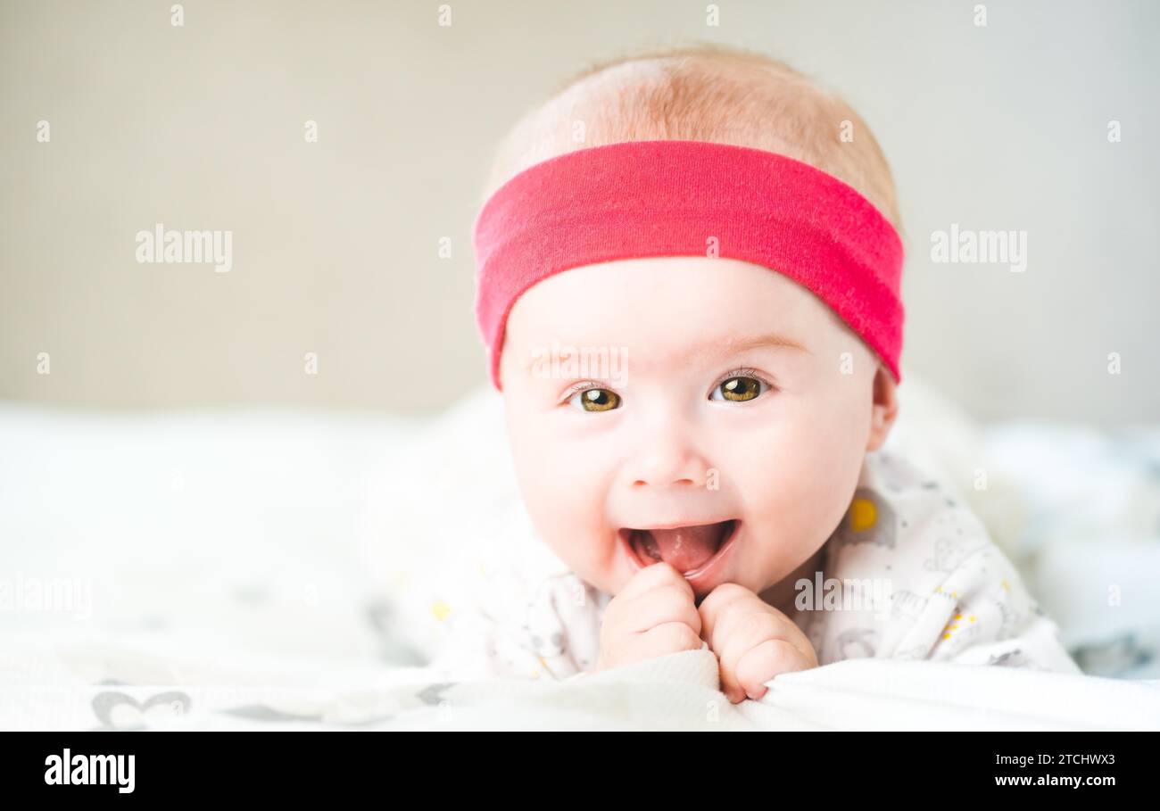 Adorable baby girl with red head band looking towards camera and smiling. Health concept. 6 months old baby. Copy space Stock Photo