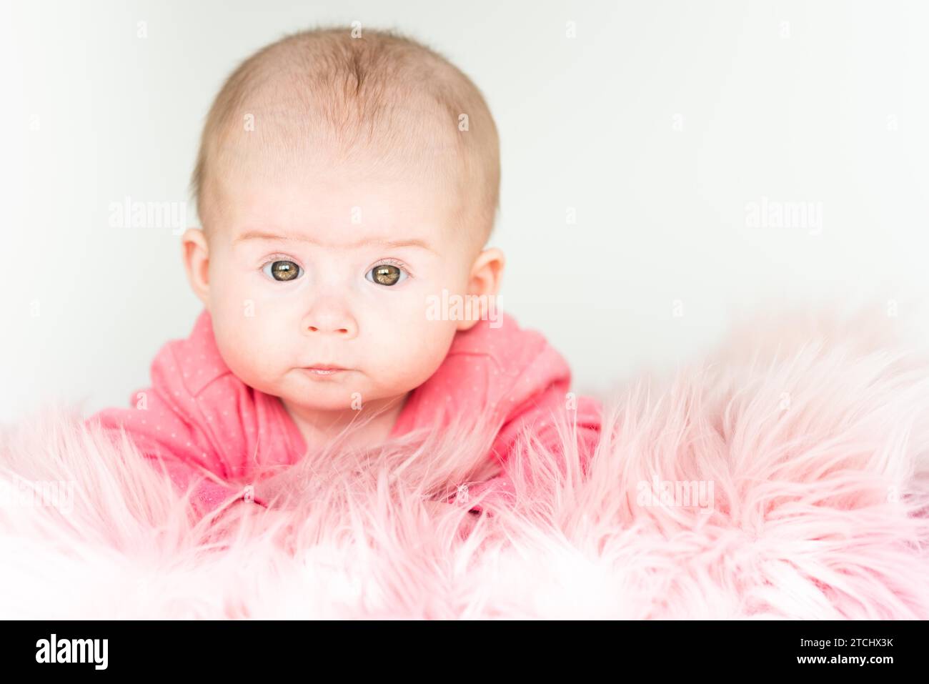 Cute baby girl lying on furry blanket on the bed at home and watching