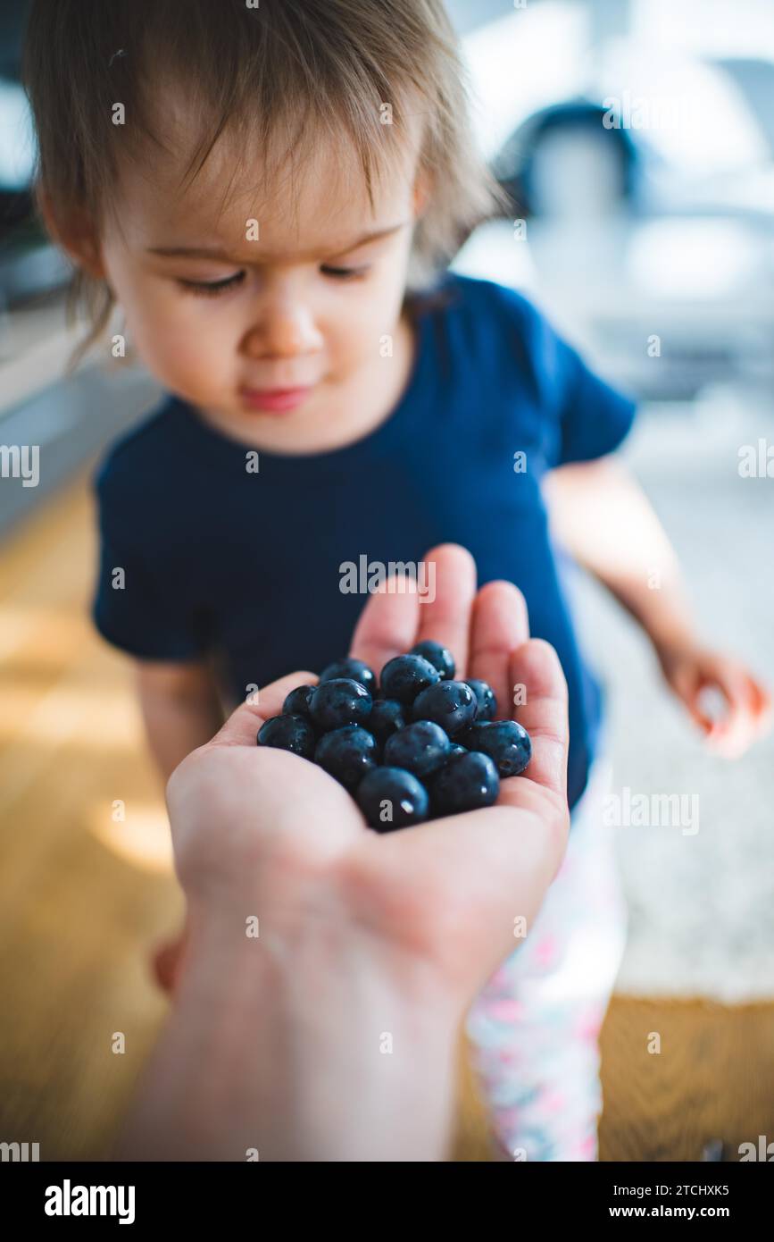 Adorable baby happy to see hand full with blueberries. Portrait of 1, 2