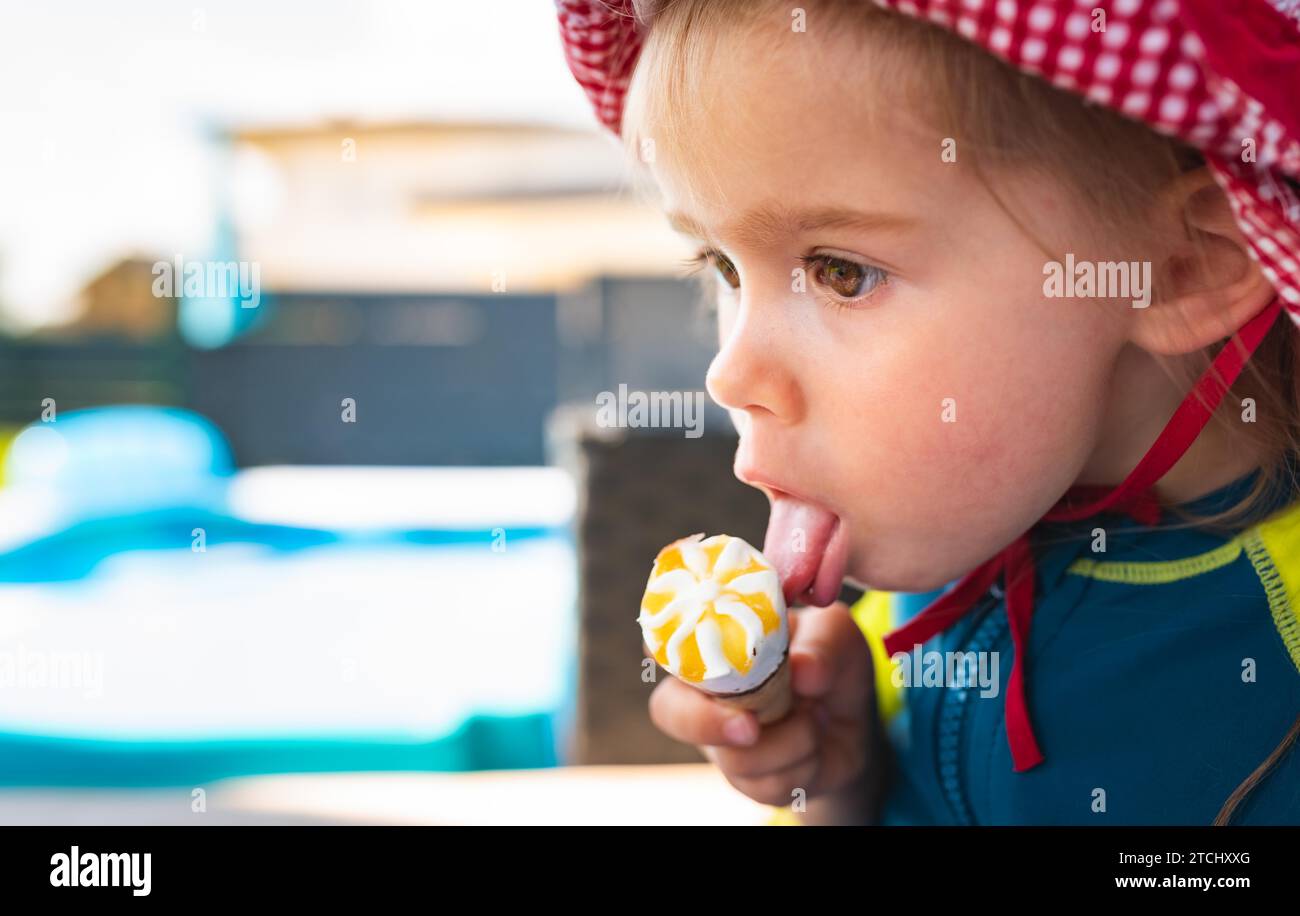 Portrait little child with big eyes licking icecream in summer. 2 year old baby girl. Kids eating sweets Stock Photo