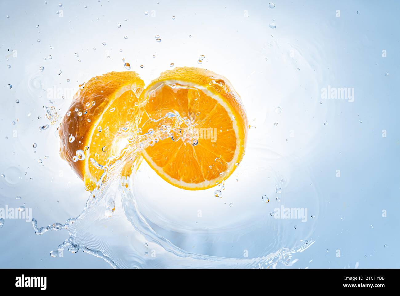 Two halves of orange fruit splashing into clear water, isolated on light blue background. Health food concept Stock Photo