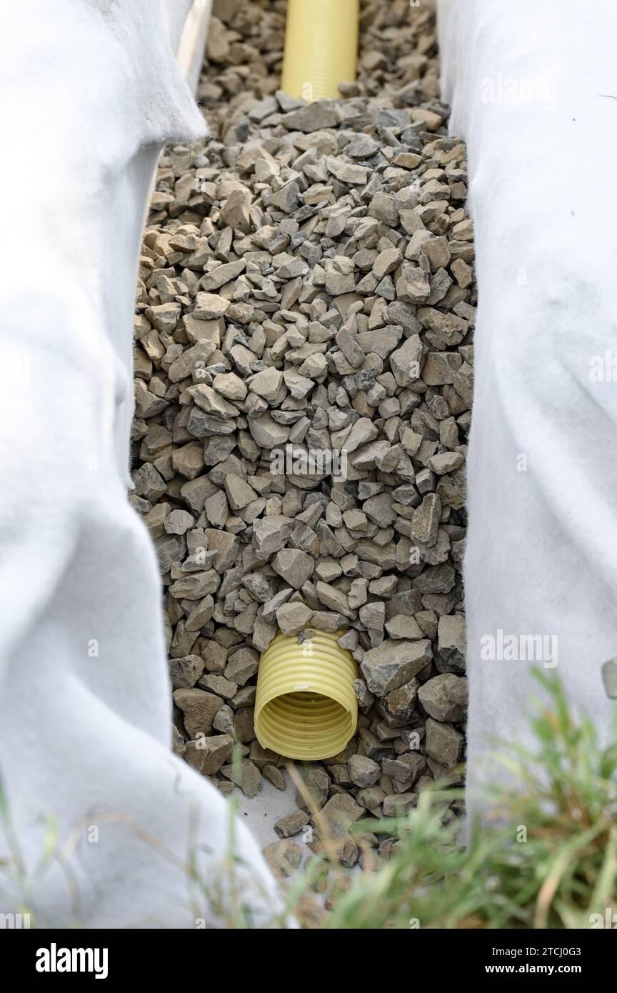 Yellow corrugated pipe with perforation in a trench with crushed stone and geotextile. Drainage works for the removal of ground water in the field. Stock Photo