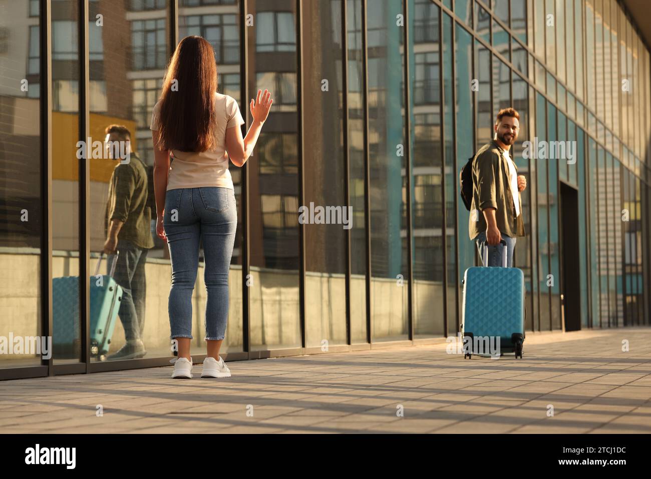 Long-distance relationship. Woman waving to her boyfriend with luggage ...