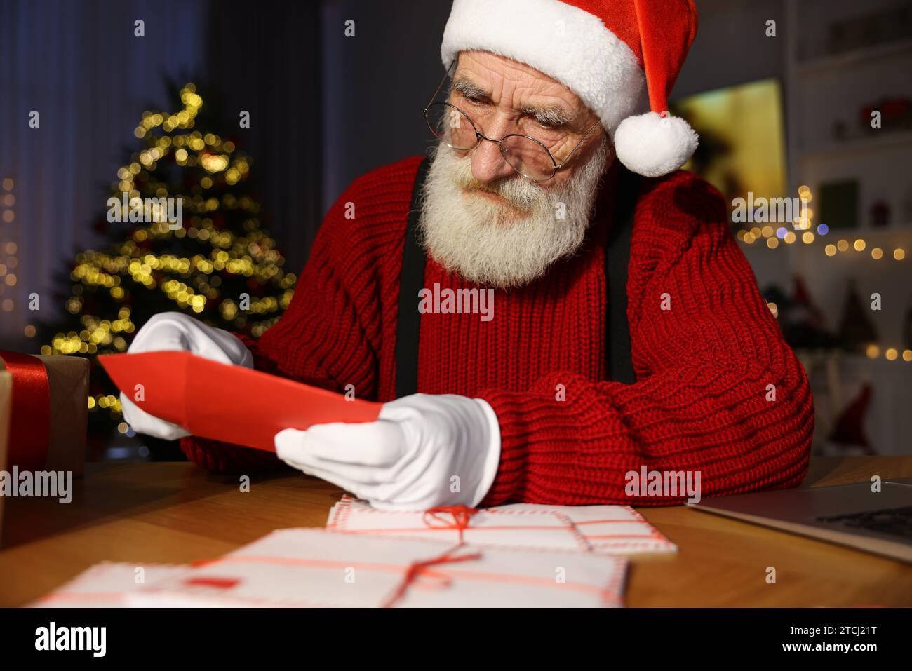 Santa Claus opening letter at his workplace in room decorated for Christmas Stock Photo