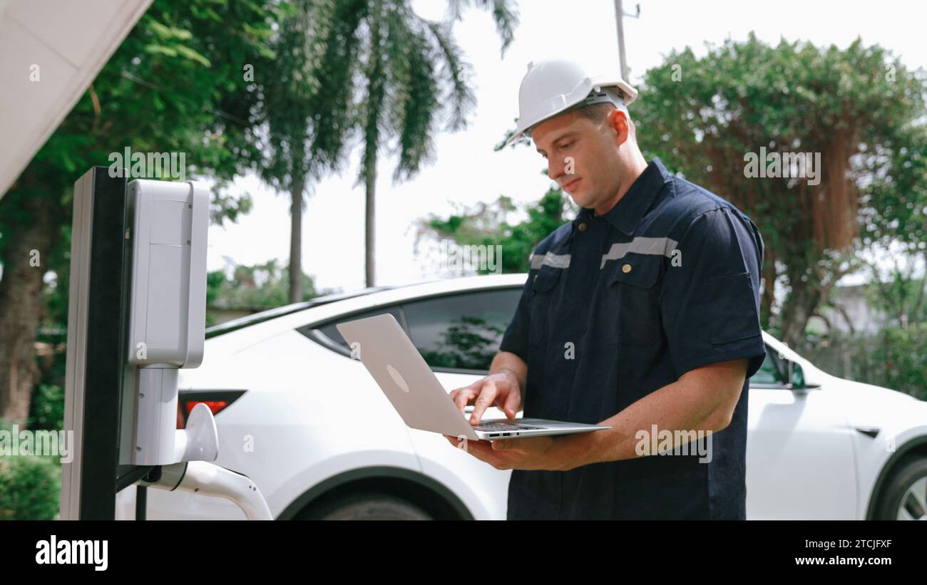 Qualified technician working on home EV charging station installation, making troubleshooting and configuration setup on charging system with laptop Stock Photo