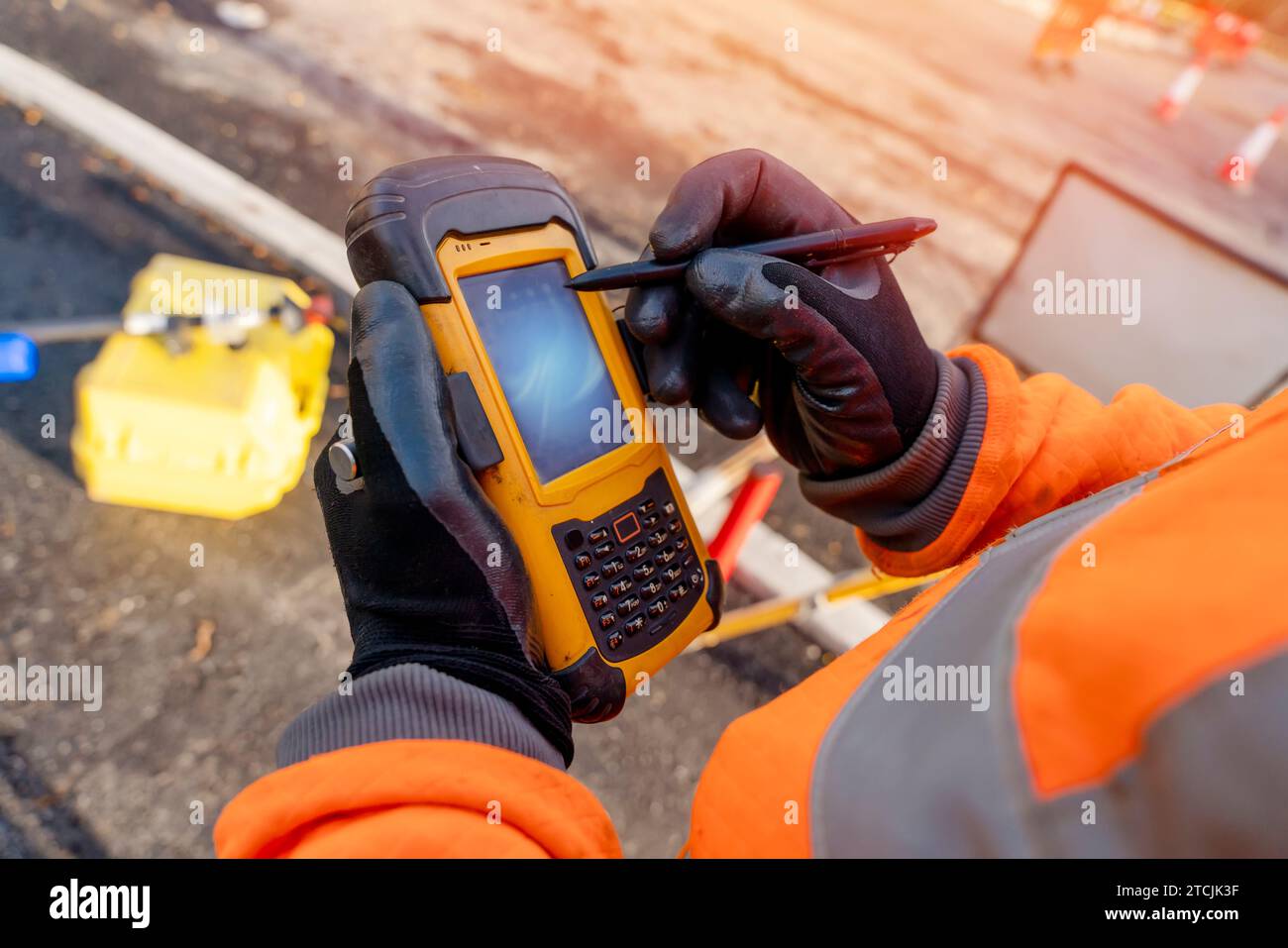 Site engineer operating his touch screen controller instrument during roadworks. Builder using touch screen controller to control total positioning st Stock Photo