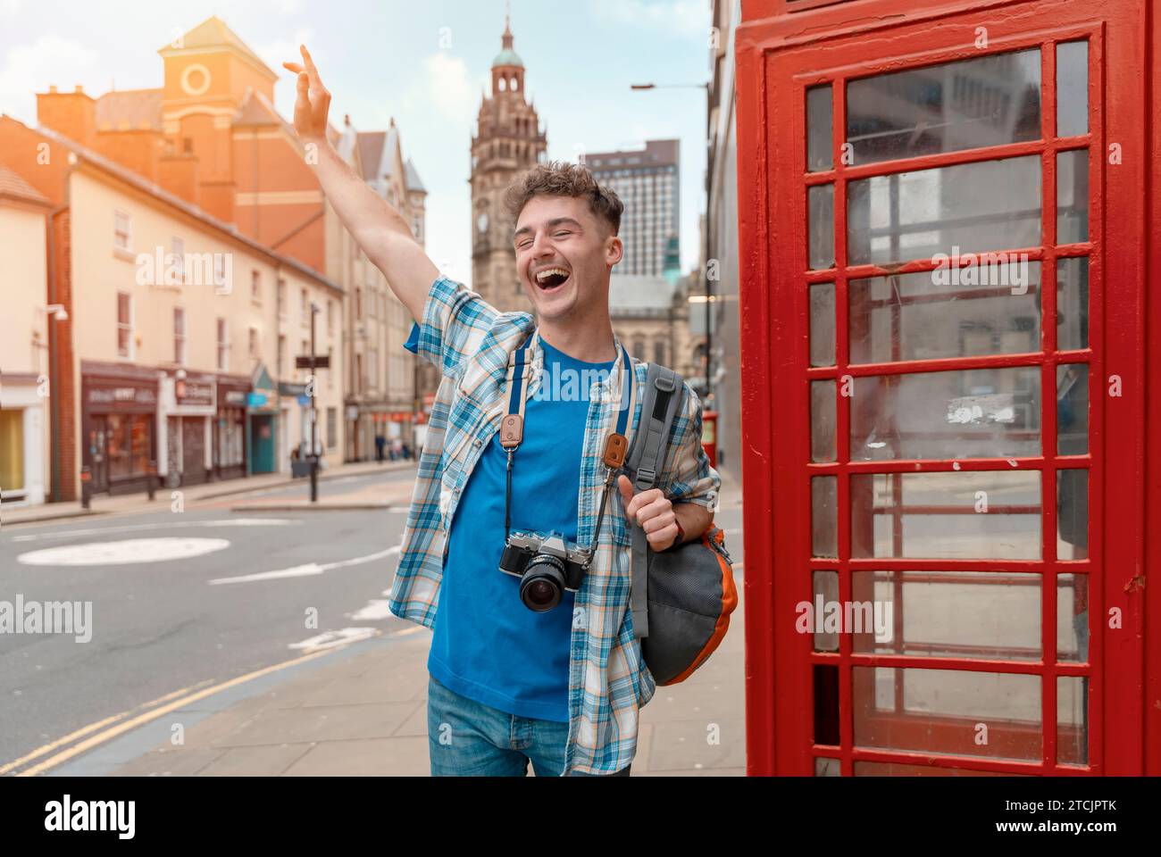 Outdoor portrait of man using a camera and taking photos against a red phonebox in the city of England Enjoying travel concept Stock Photo
