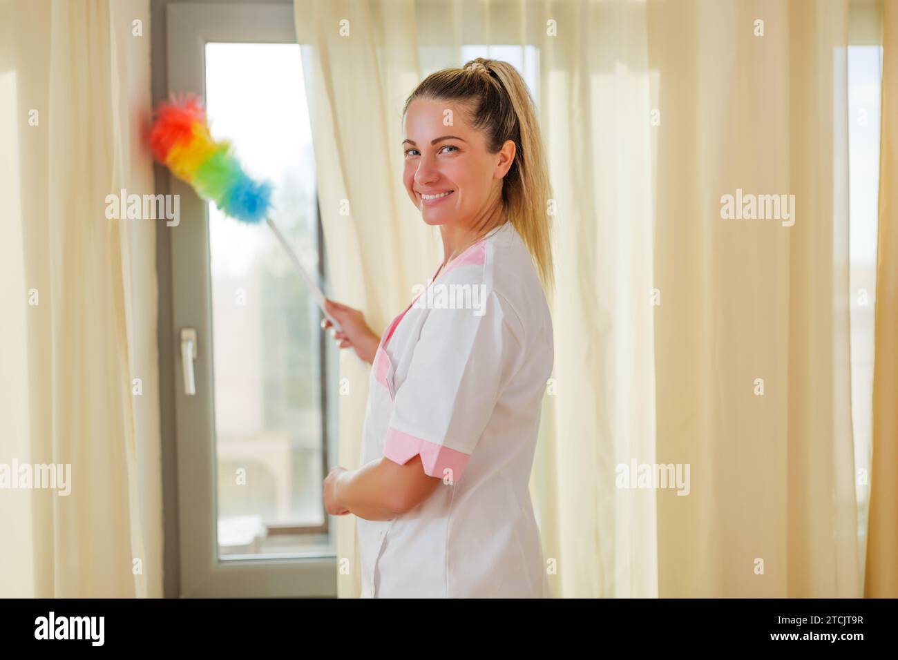 Image of beautiful hotel maid cleaning room with a duster. Stock Photo
