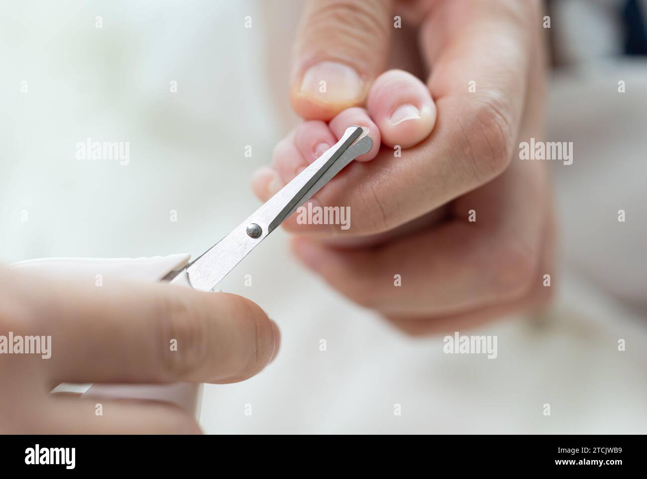 Mother's hands cutting newborn baby's toenails with scissors Stock