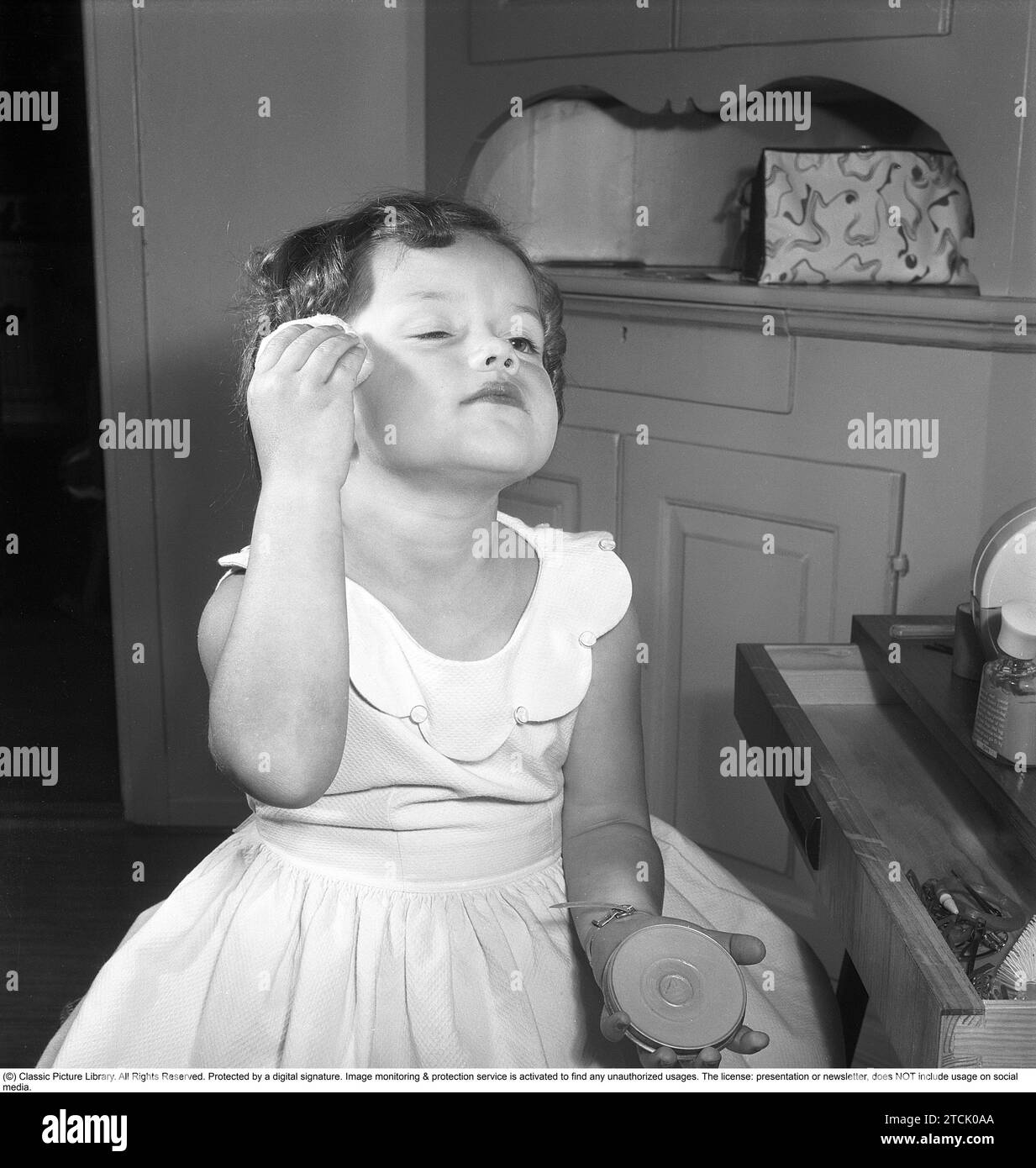 In the 1950s. A little girl is putting on makeup, using a powder on her face. 1956. Kristoffersson ref BS96-11 Stock Photo