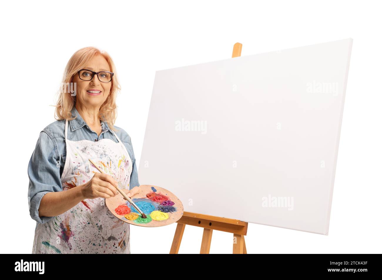 Female artist standing next to a painting canvas and holding a brush ...