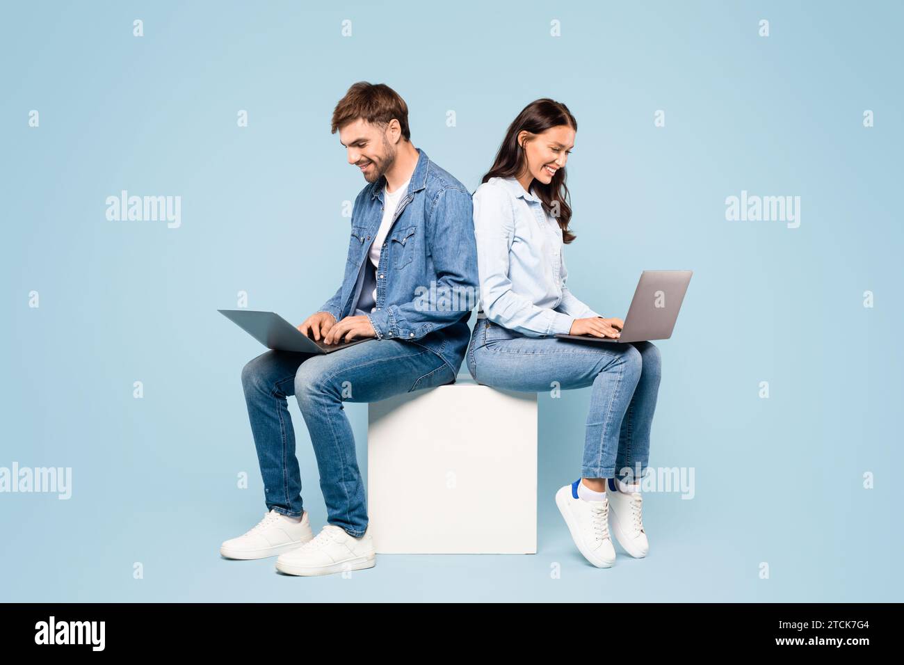 Focused couple on cube using laptops in denim attire Stock Photo