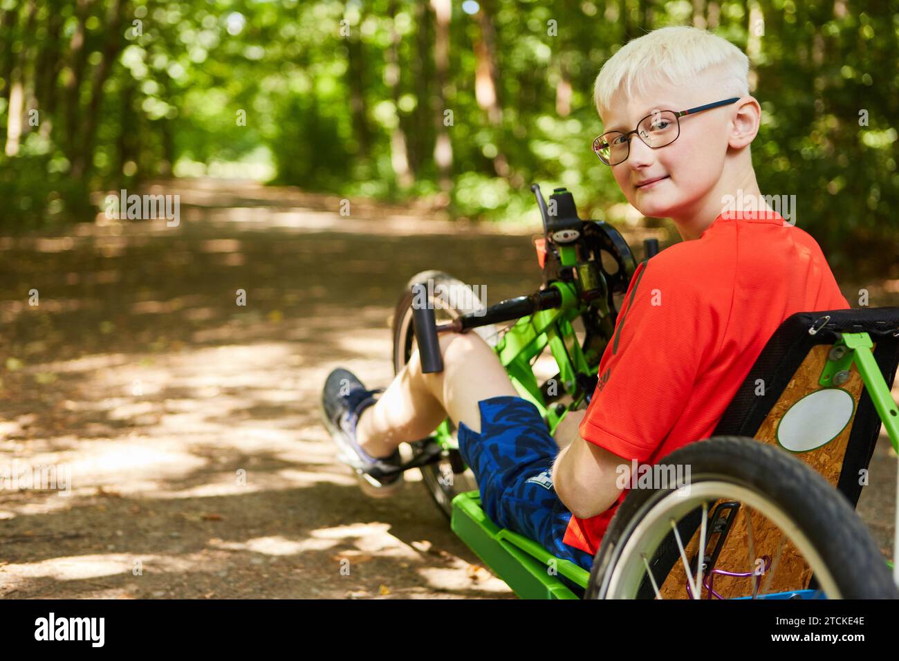 Portrait of smiling blond boy with disability sitting on recumbent bike at forest Stock Photo