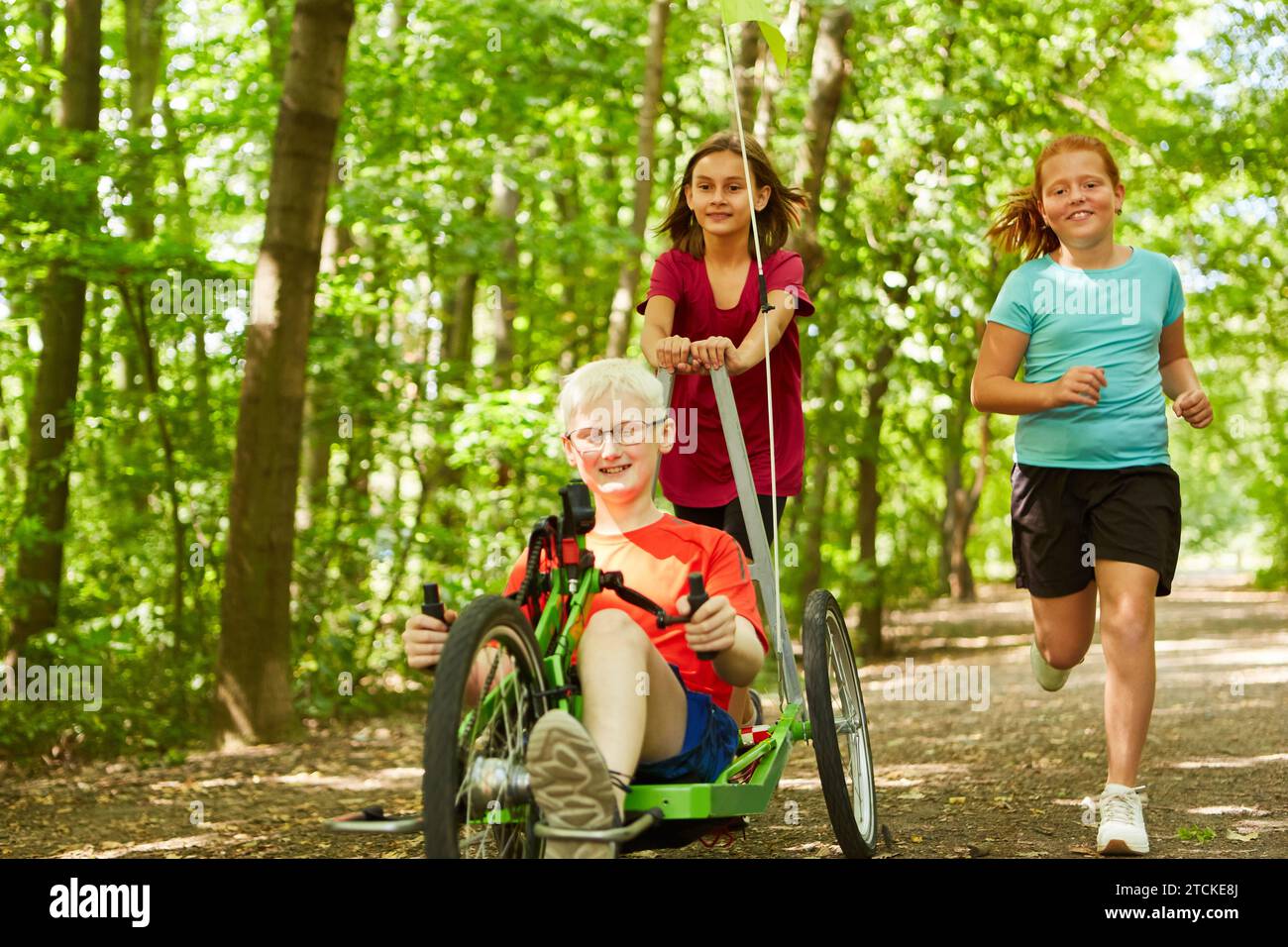Happy female friends playing with handicapped boy riding recumbent bike at forest Stock Photo