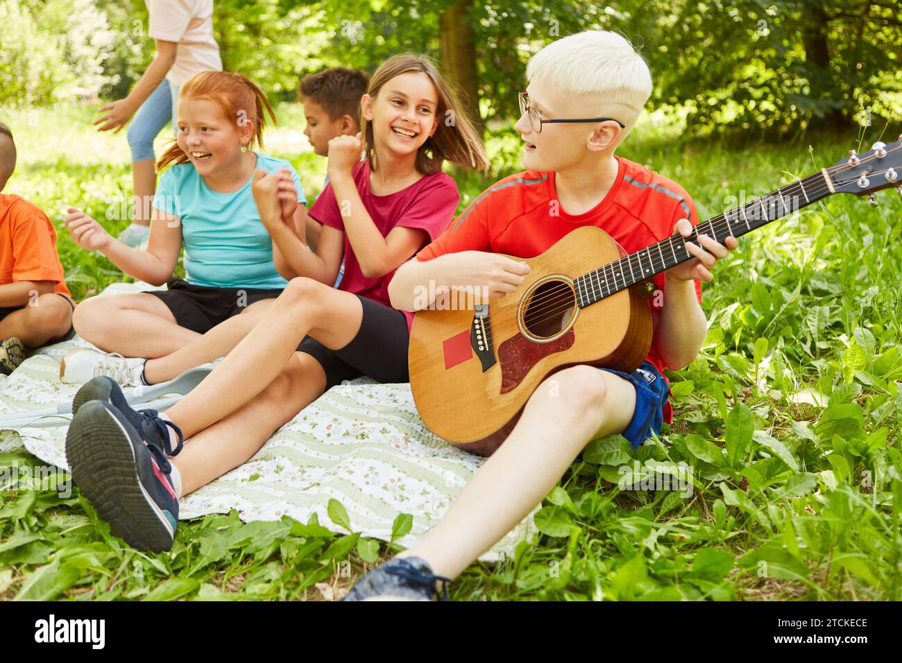 Disabled boy playing guitar while sitting down with friends on blanket during picnic at park Stock Photo