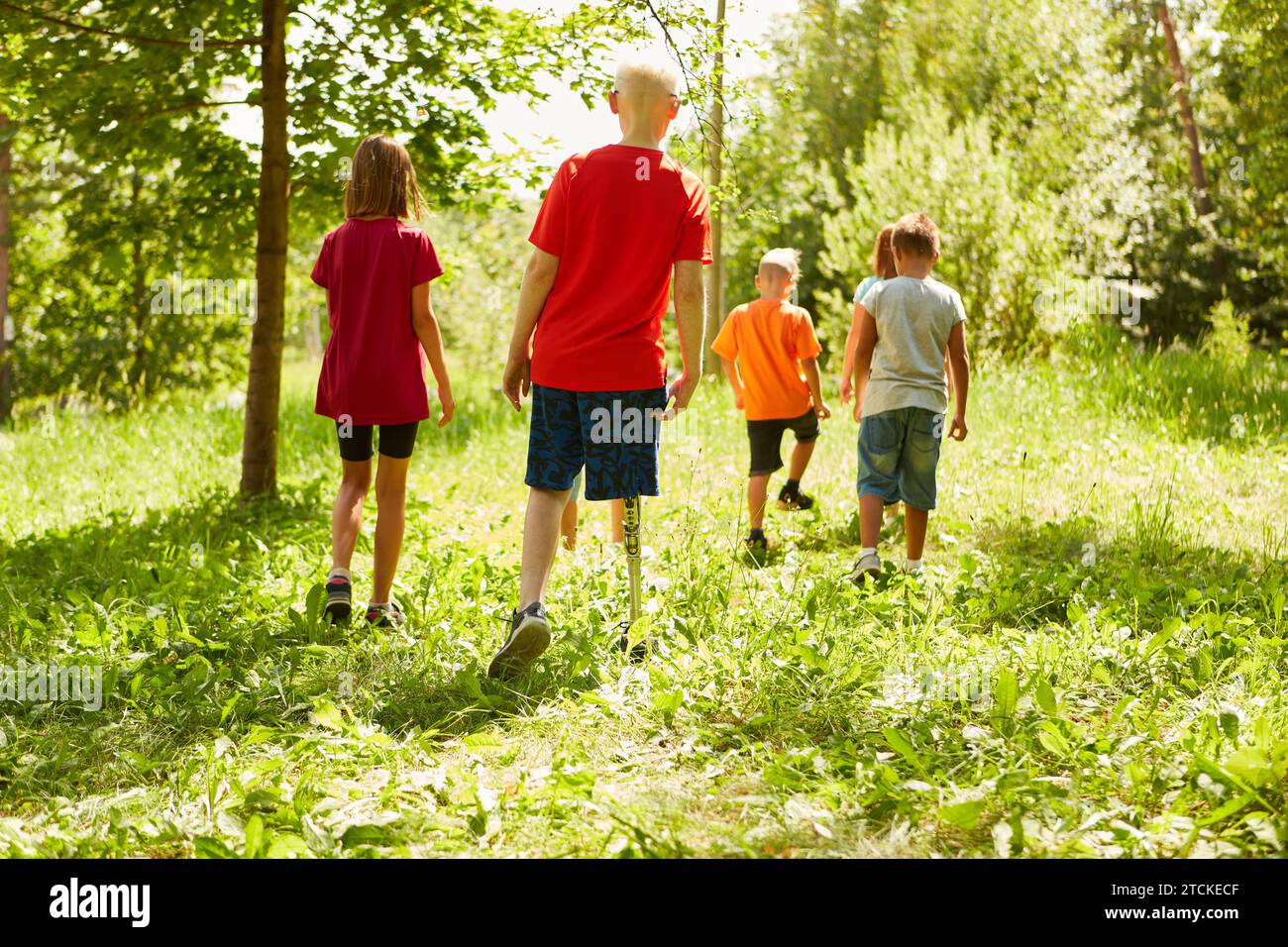 Rear view full length of handicapped boy walking with friends on grass at park Stock Photo