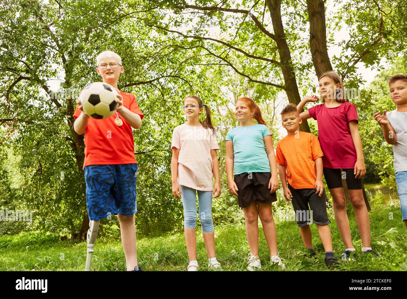 Disabled boy playing soccer while standing with male and female friends at park Stock Photo