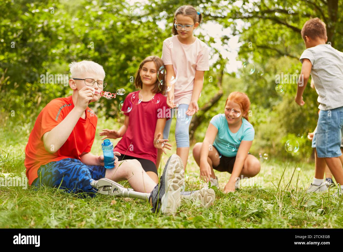 Disabled boy blowing bubbles with friends while sitting at park Stock Photo