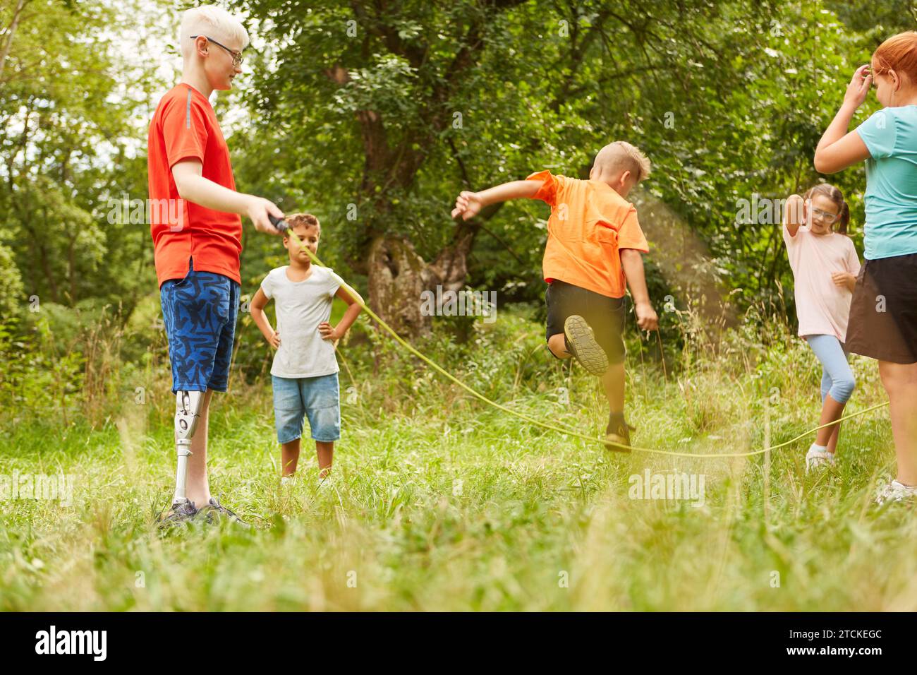 Rear view of boy jumping over skipping rope while playing with friends at park Stock Photo