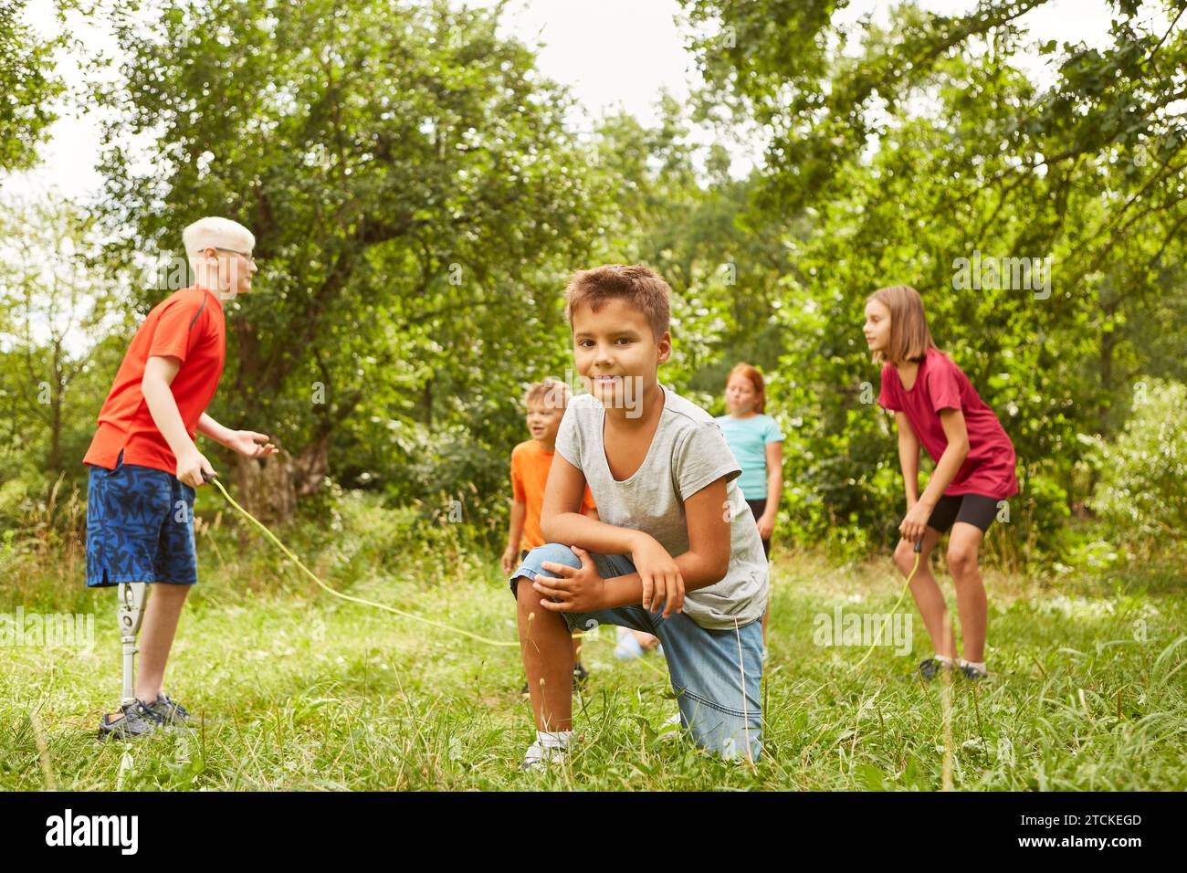 Portrait of smiling boy kneeling on grass with friends playing in background at park Stock Photo