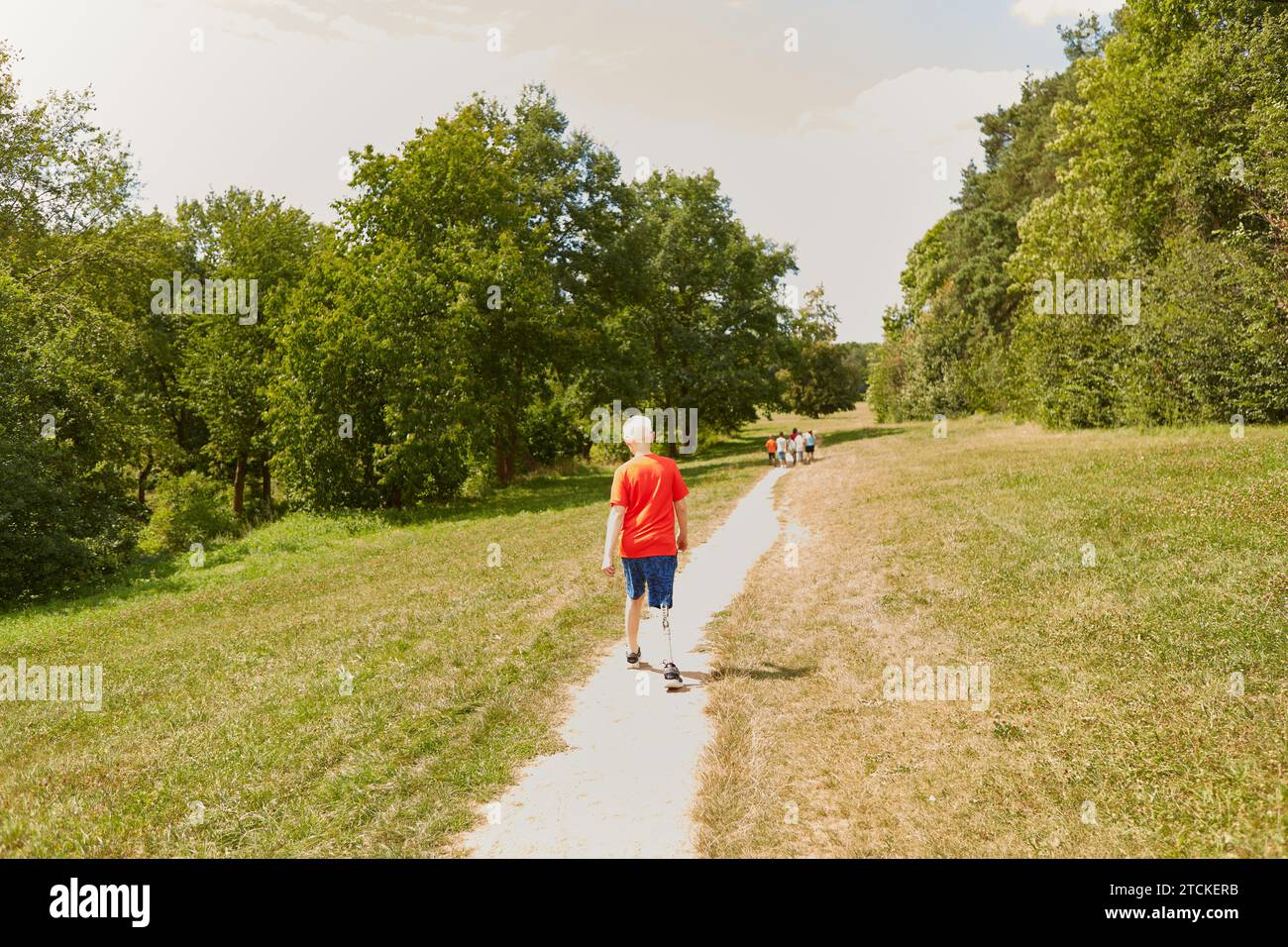 Rear view full length of disabled boy walking on footpath at park Stock Photo