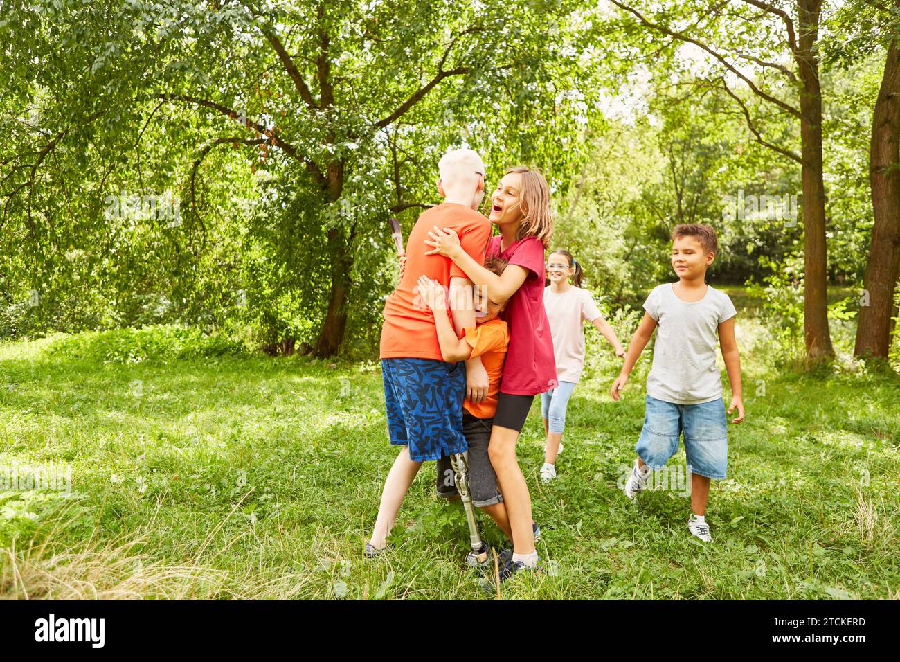 Happy children embracing disabled male friend standing at park Stock Photo