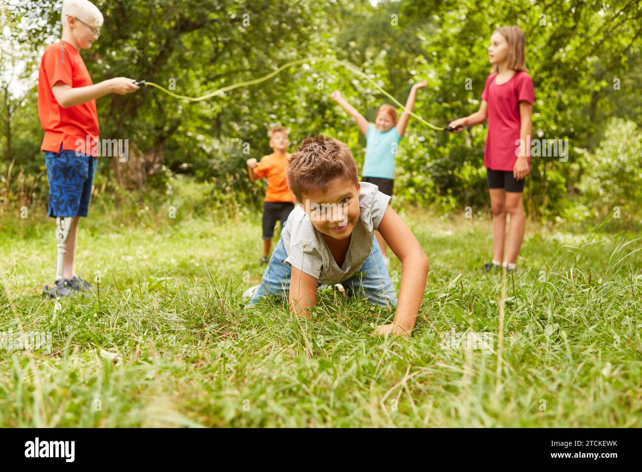 Portrait of boy crawling on grass with friends playing in background at park Stock Photo