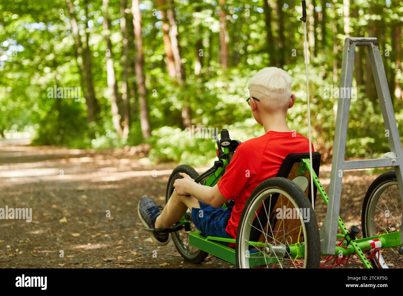 Rear view of handicapped boy riding recumbent bike on footpath at forest Stock Photo