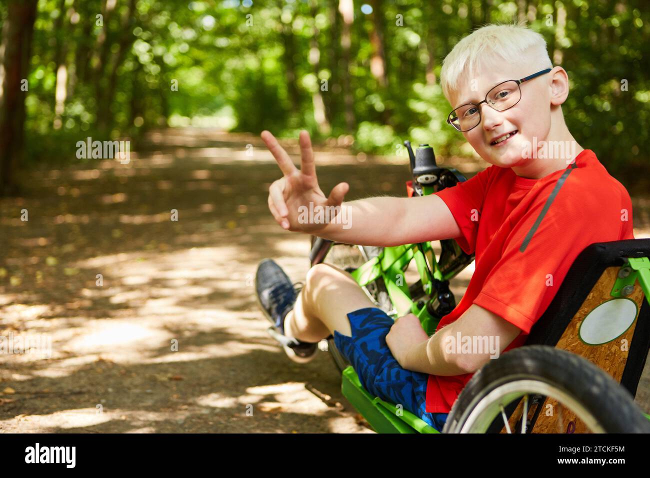 Portrait of smiling boy showing peace sign while sitting on recumbent bike at forest Stock Photo