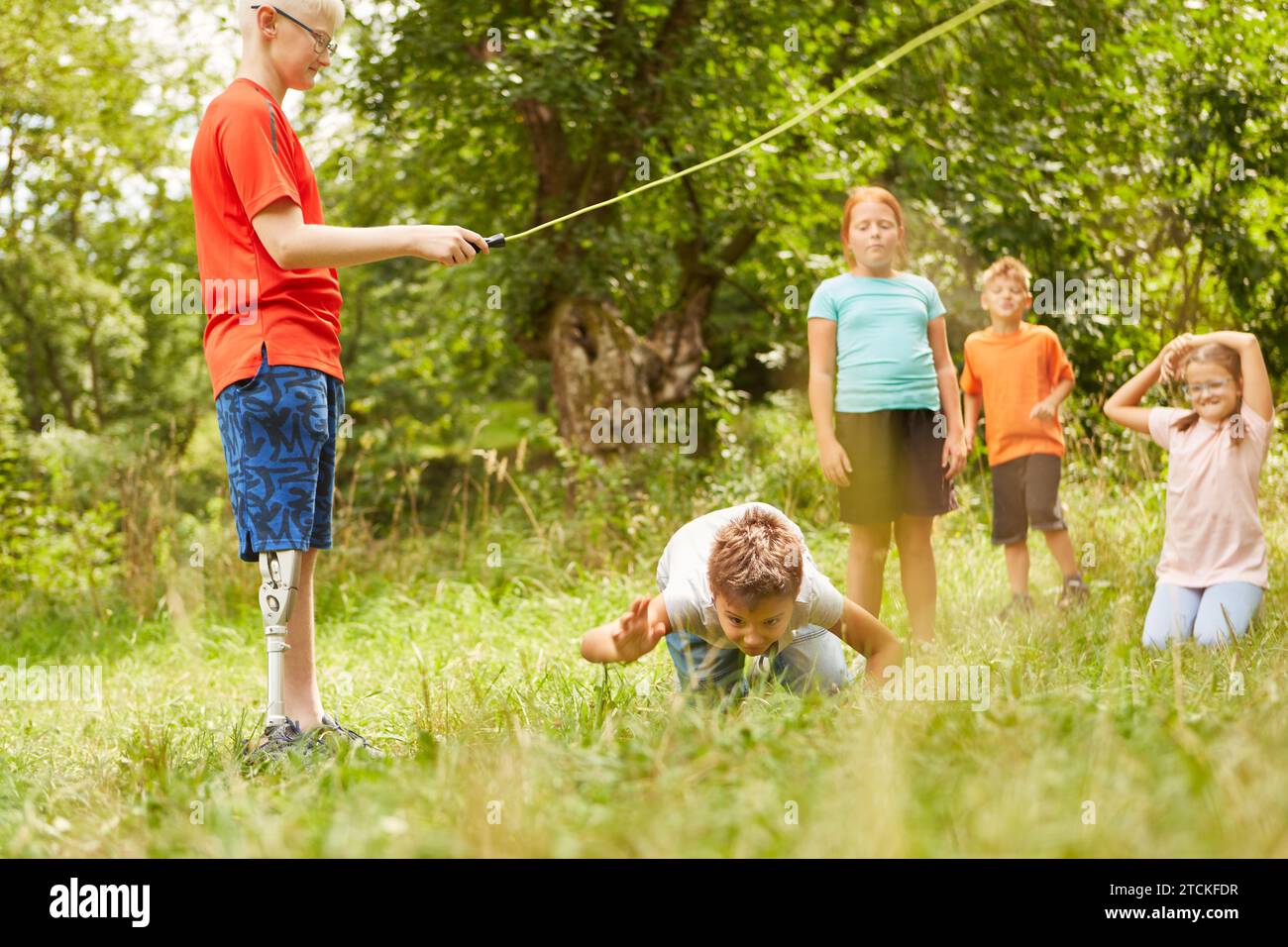 Boy crawling under skipping rope while playing with friends on grass at park Stock Photo