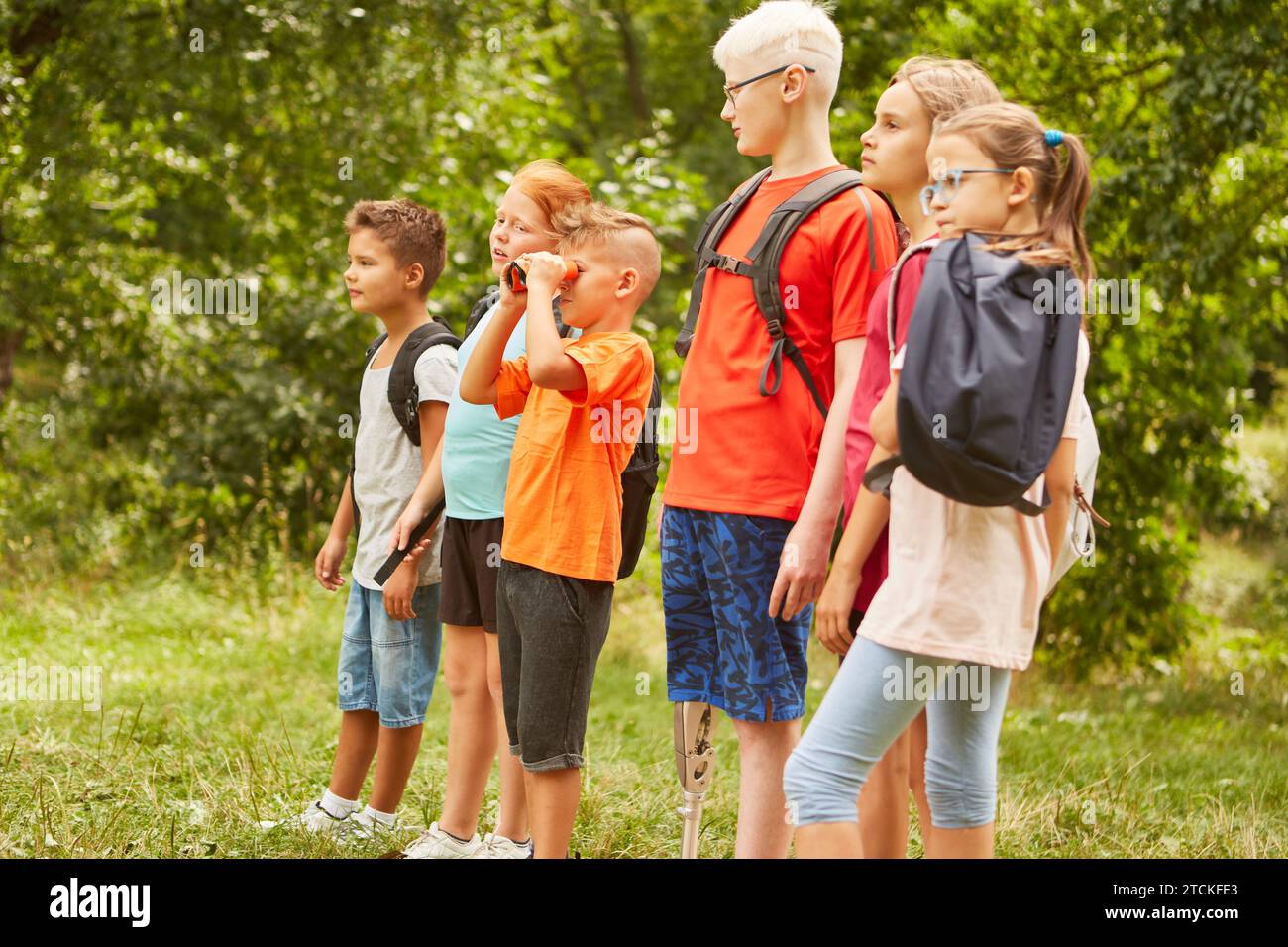 Curious boy looking through binoculars while standing with friends at park Stock Photo