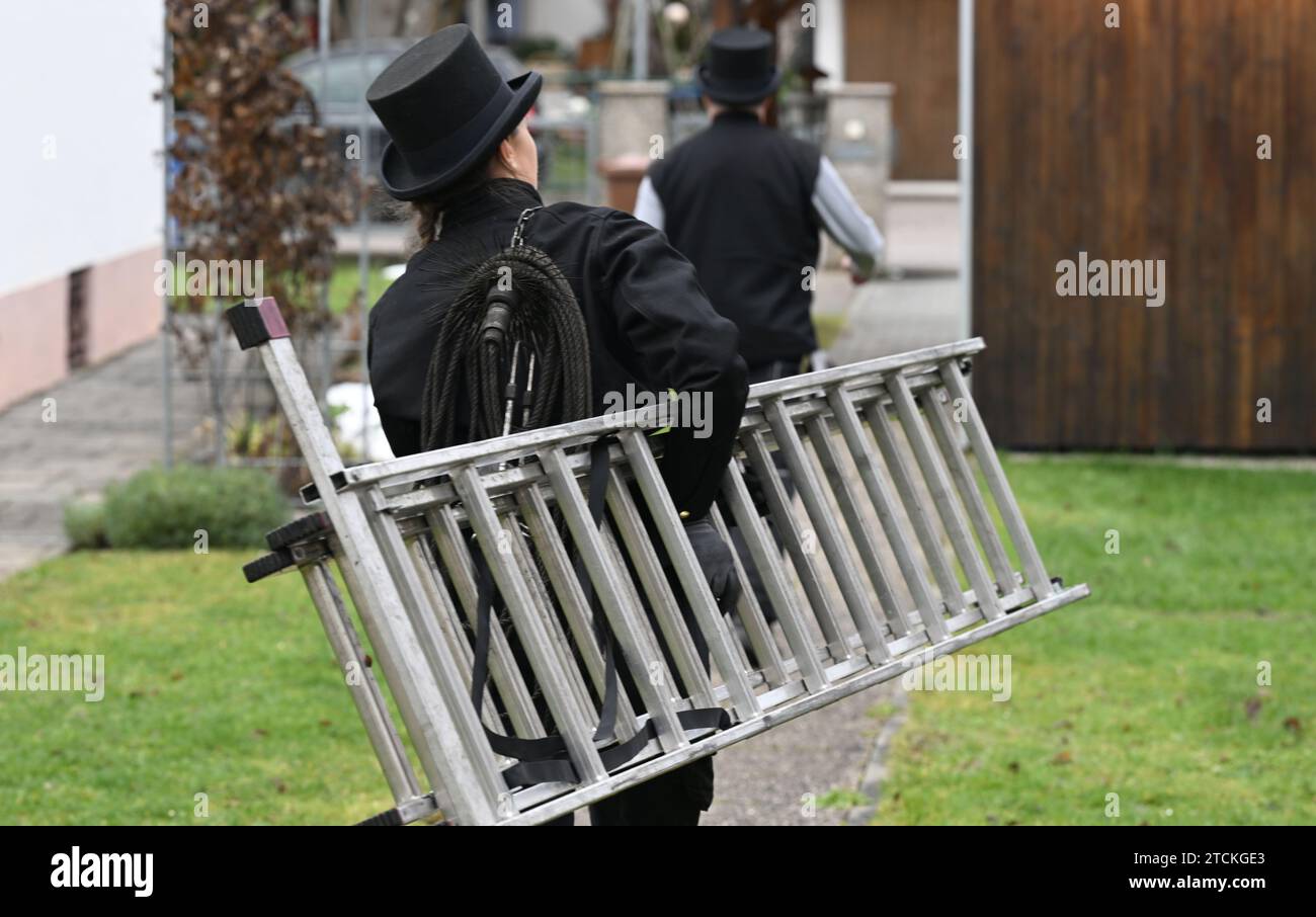 Munich, Germany. 13th Dec, 2023. Chimney sweep Diane Löbel walks through the garden of a detached house with a ladder. From January, only heating systems based on 65 percent renewable energy may be installed in new buildings in new development areas. In many cases, this is likely to be a heat pump. Credit: Felix Hörhager/dpa/Alamy Live News Stock Photo