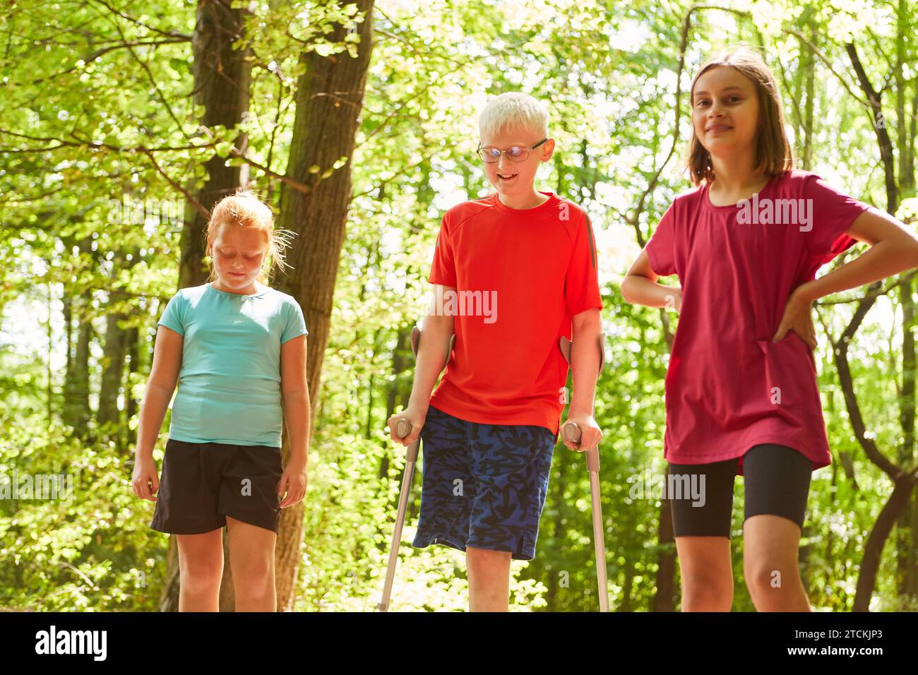 Female friends standing with boy walking with crutches in forest Stock Photo