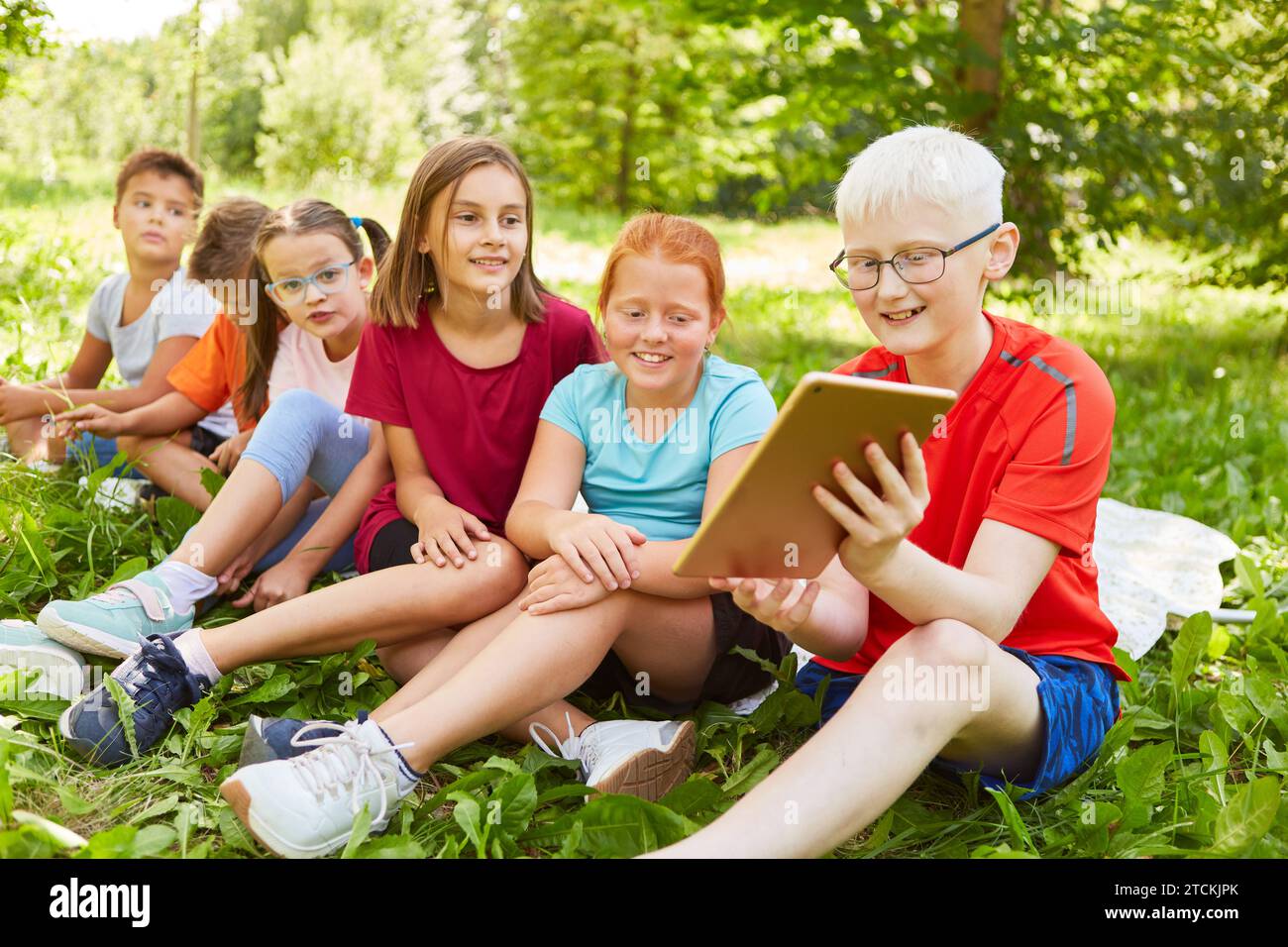 Smiling boy sharing tablet PC with male and female friends while sitting at park Stock Photo