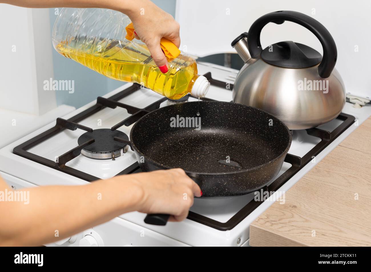 housewife pours sunflower oil into a frying pan. cooking fried food at home. frying oil. fry pancakes Stock Photo