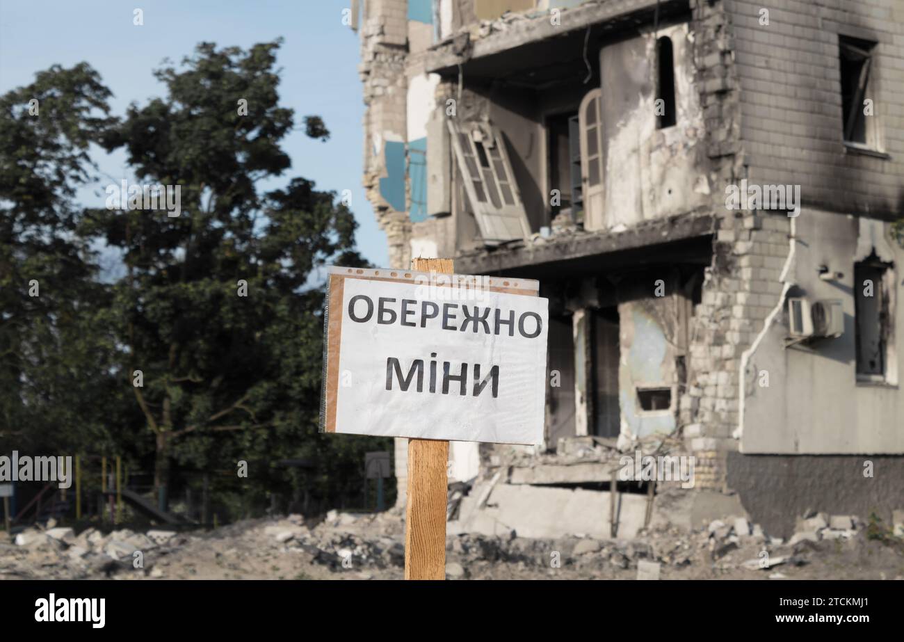 The sign Beware of mines on the background of a destroyed residential building. as a result of a missile attack by the Russian army. Stock Photo