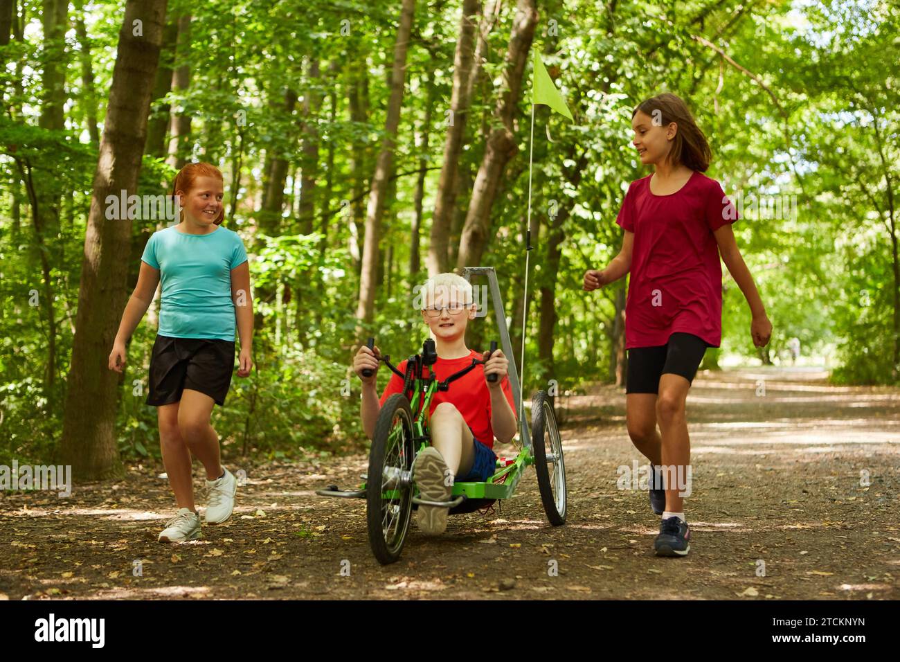 Boy riding recumbent bike with female friends walking on footpath at park Stock Photo