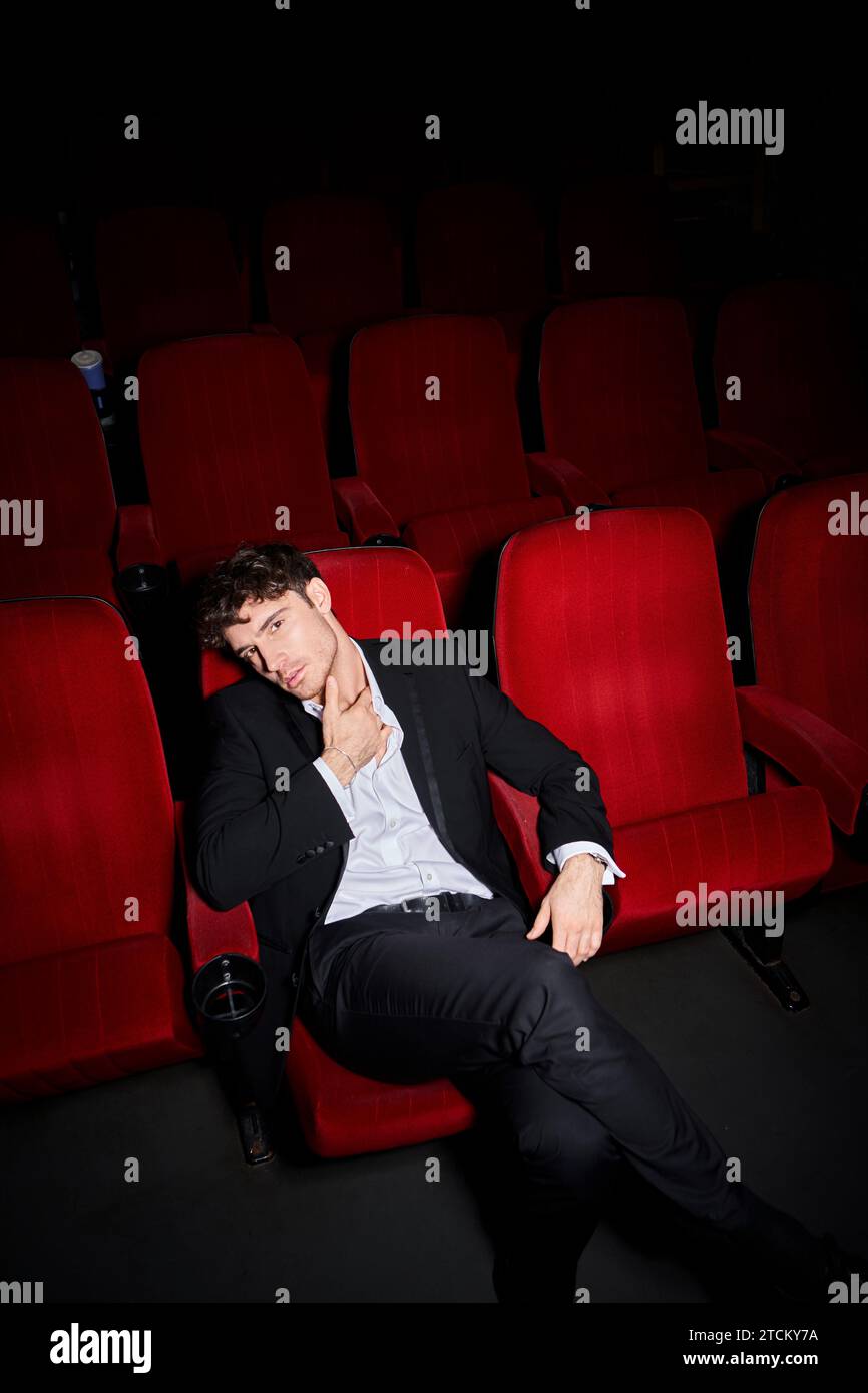 appealing elegant male model with dapper style enjoying movie at cinema and looking at camera Stock Photo