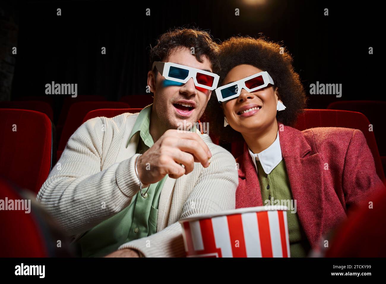 handsome man eating popcorn next to his jolly african american