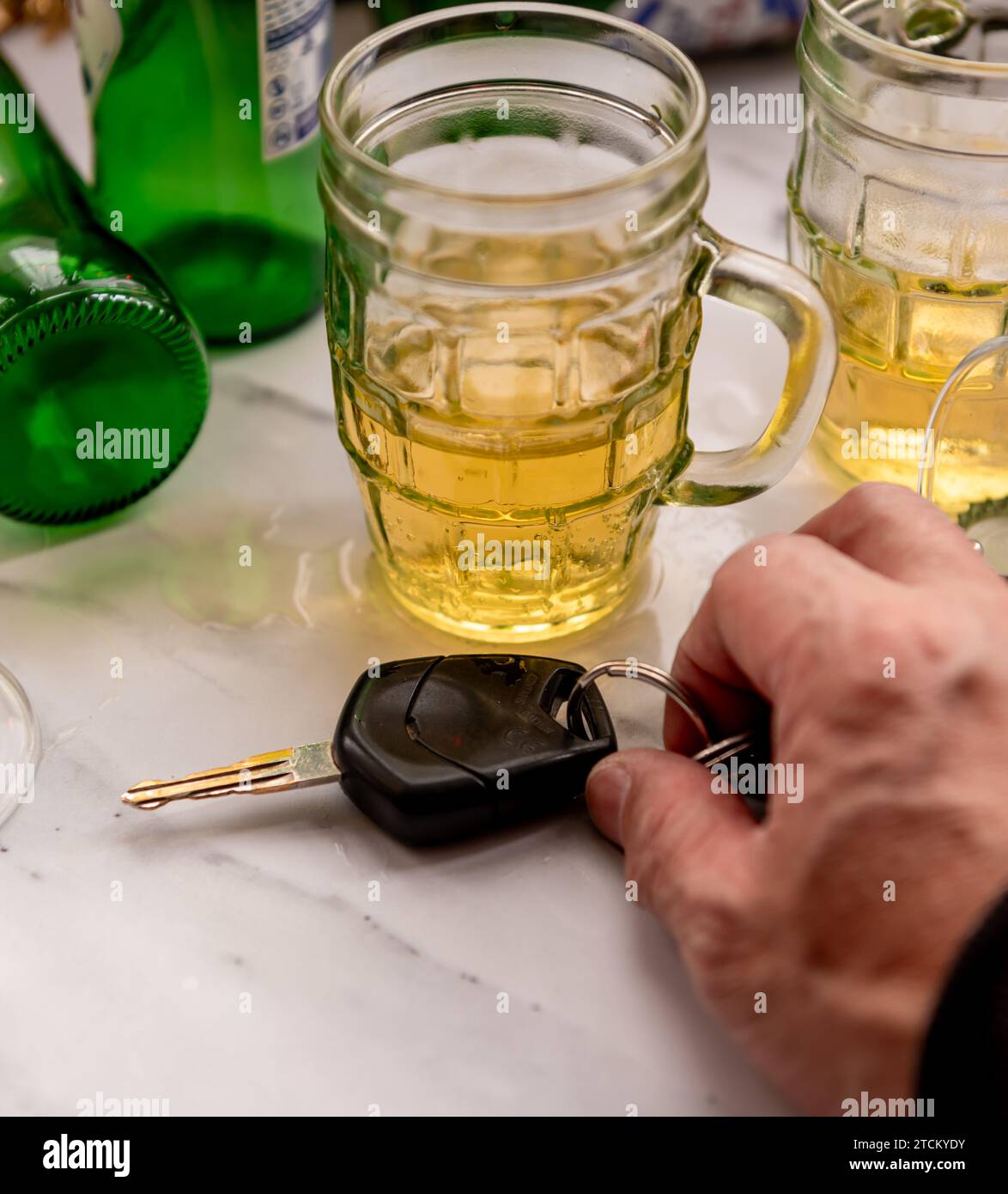 A drink drive concept with a table full of alcoholic drinks and a person picking up a set of car keys to drive. Stock Photo