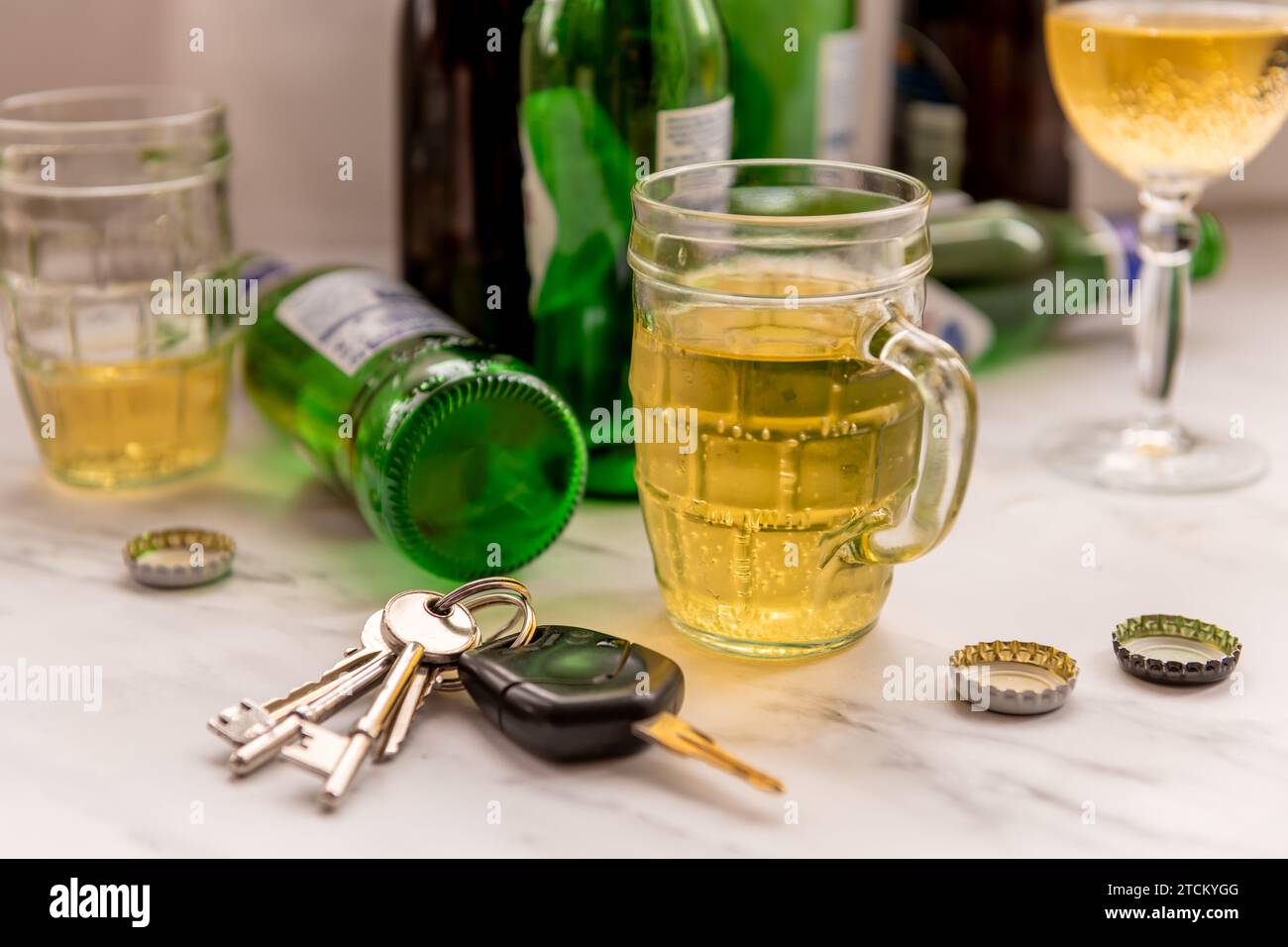 A set of car keys on a table full of glasses of alcoholic drinks and bottles. Drink driving concept. Stock Photo