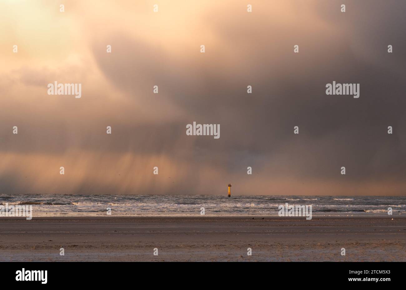 Yellow measuring post in the North Sea, close to the beach, contrasting with dark clouds from which rain falls. Stock Photo