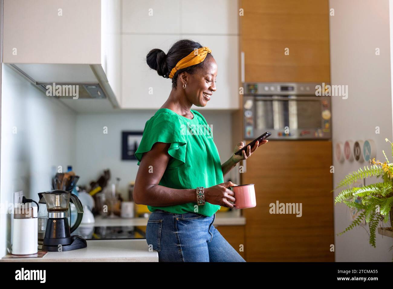 Smiling woman using smartphone in the kitchen at home Stock Photo