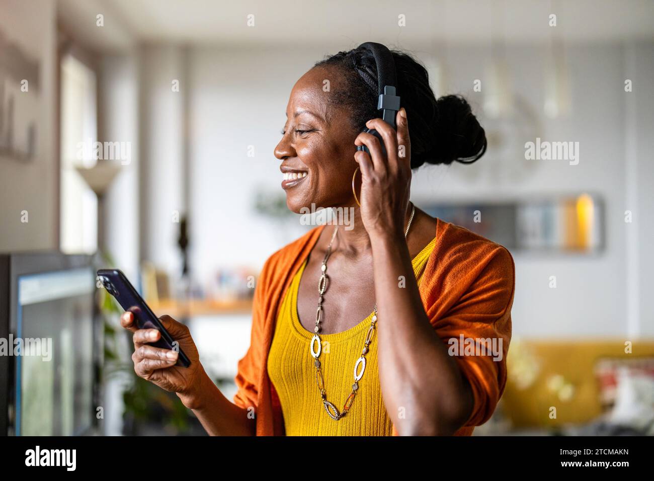 Woman listening to music with headphones connected to her smartphone in the living room at home Stock Photo