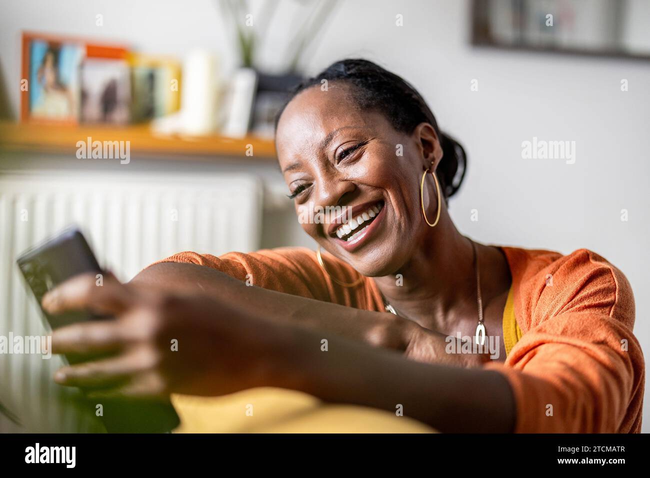 Beautiful woman using mobile phone while relaxing on sofa at home Stock Photo