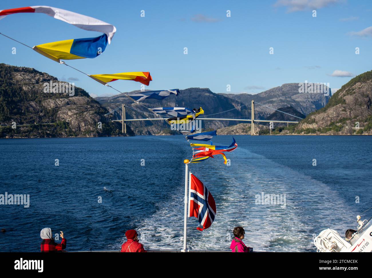Pequeñas banderas en un barco ondeando al viento y el paisaje del Fiordo de la Luz o Lysefjord con el Puente Lysefjord y la estela del barco, Stavange Stock Photo